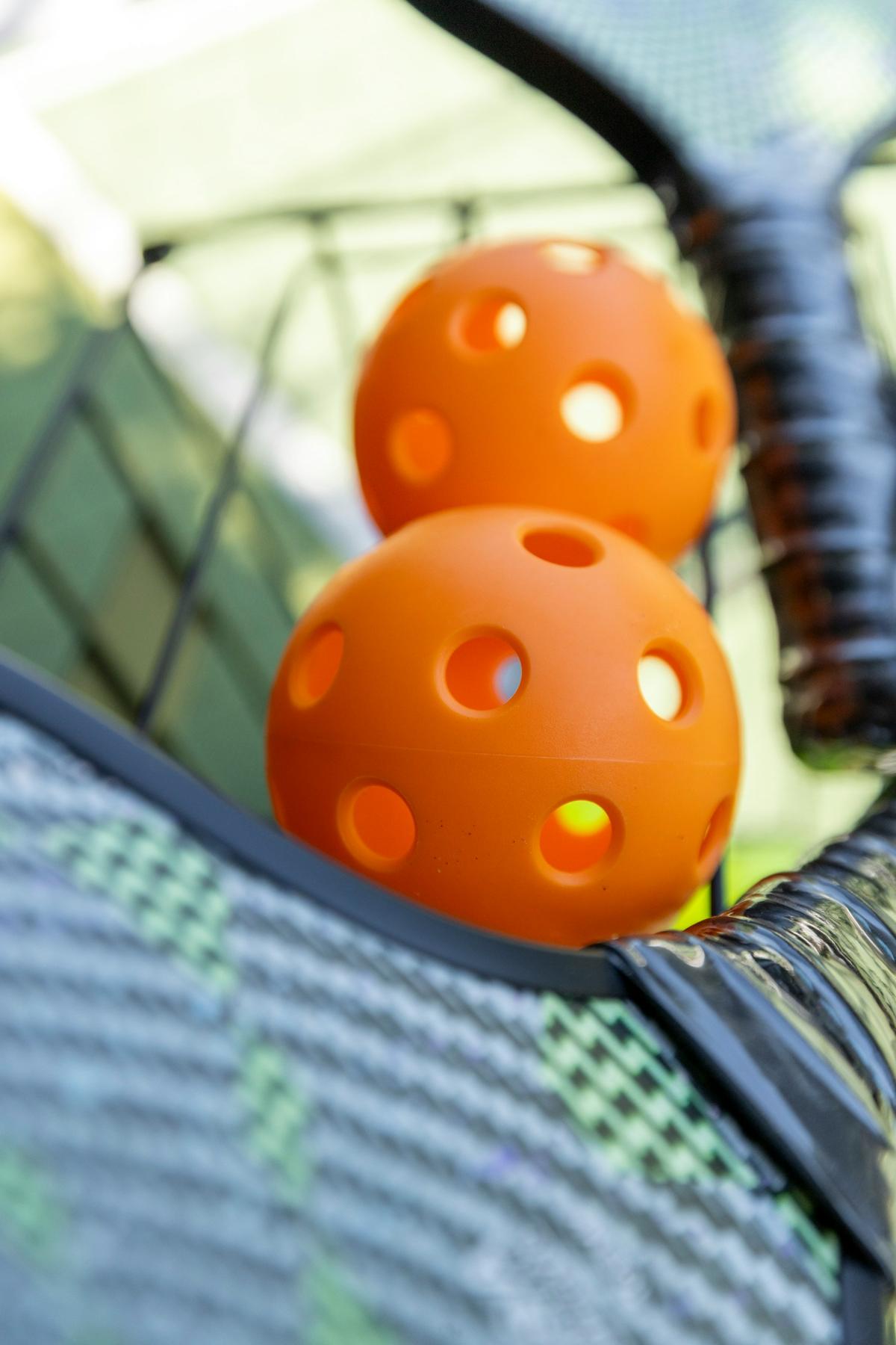 Two orange pickleballs resting against a paddle's mesh face